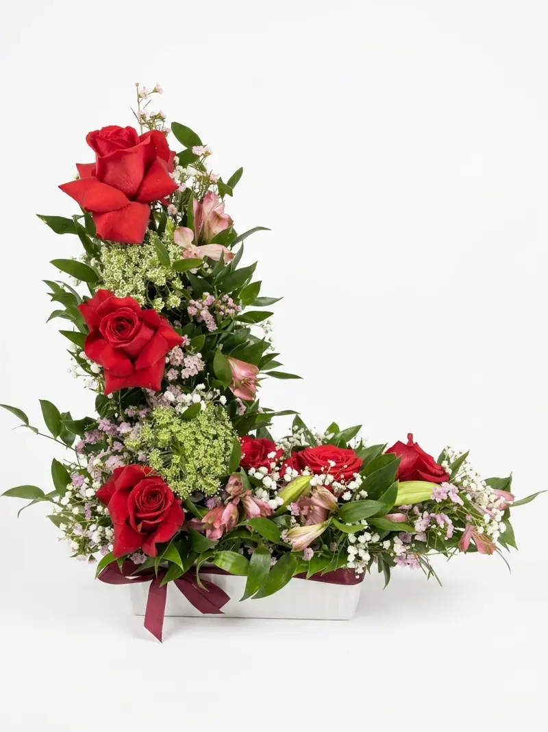 Centro de flores en forma de L con rosas rojas en jardinera blanca con lazo